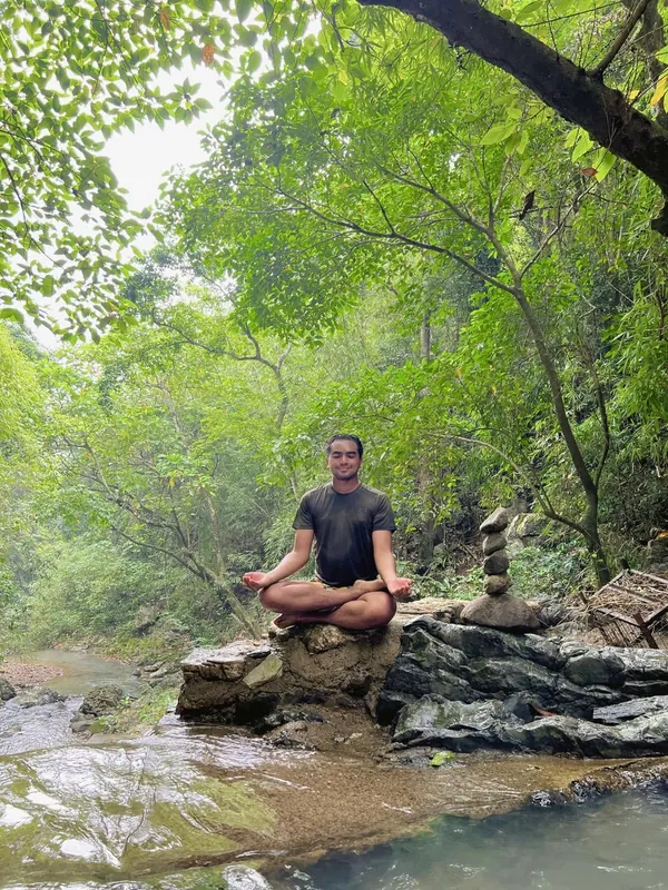 Merald Ayson meditating on a rock by a forest stream