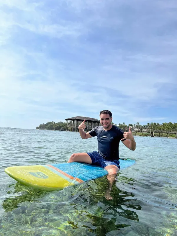 Merald Ayson sitting on a surfboard giving a thumbs up